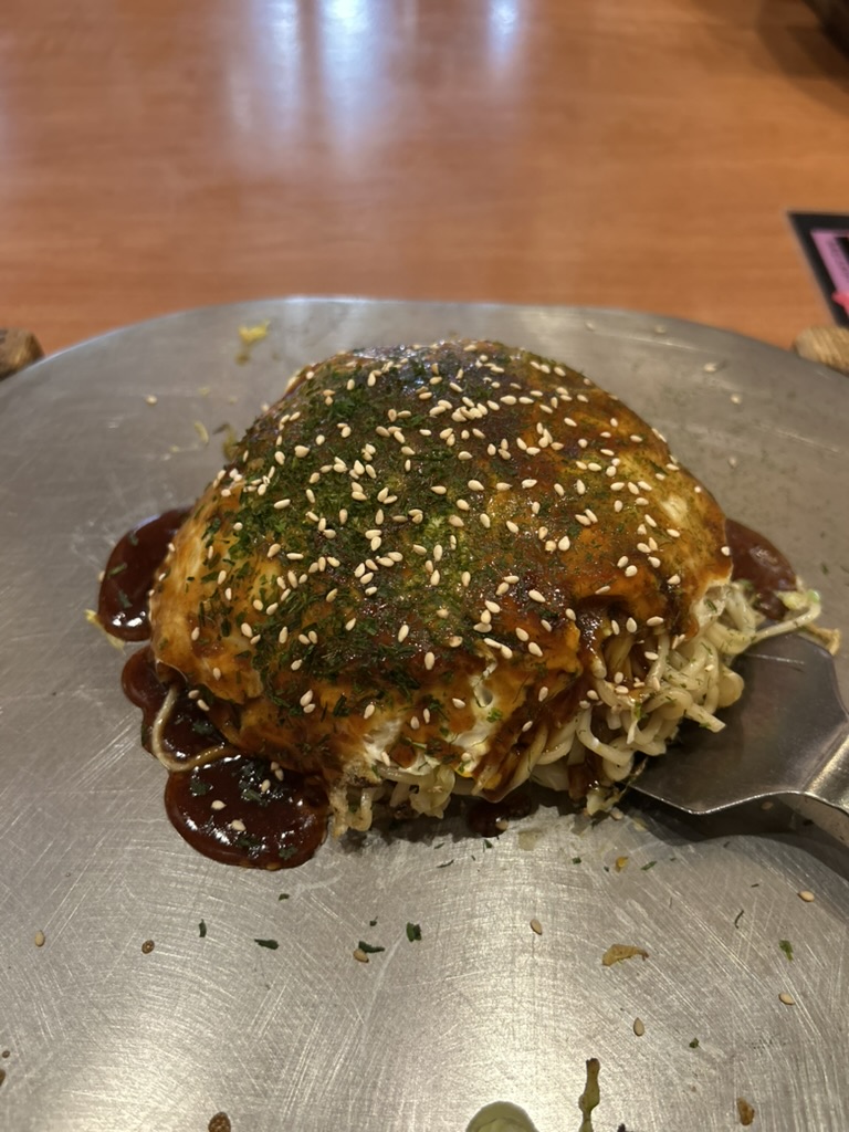 Okonomiyaki de Hiroshima sur une plaque teppan en fonte, nappé de sauce et d'aonori